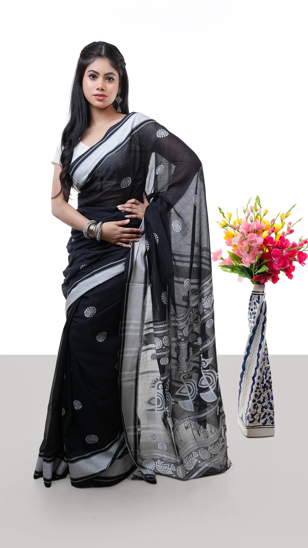 A black saree with white weave. A black Tangail saree with intricate white thread work. Crafted with soft cotton Warp and weft. Standard 5.5-meter length. Includes matching blouse piece. Tangail saree, cotton saree