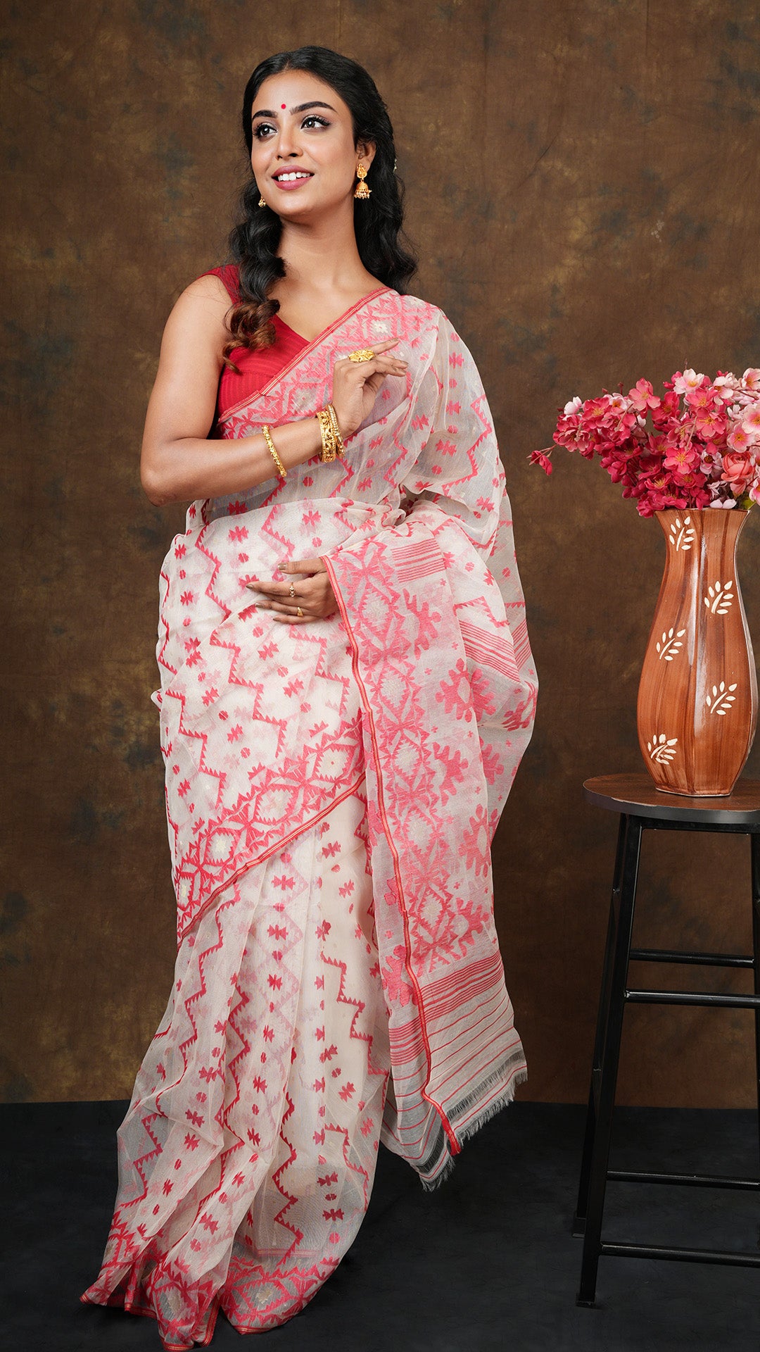 Off white muslin jamdani saree with red and golden zari woven border, pallu, and vertical body design. 5.5 meters with separate blouse piece.