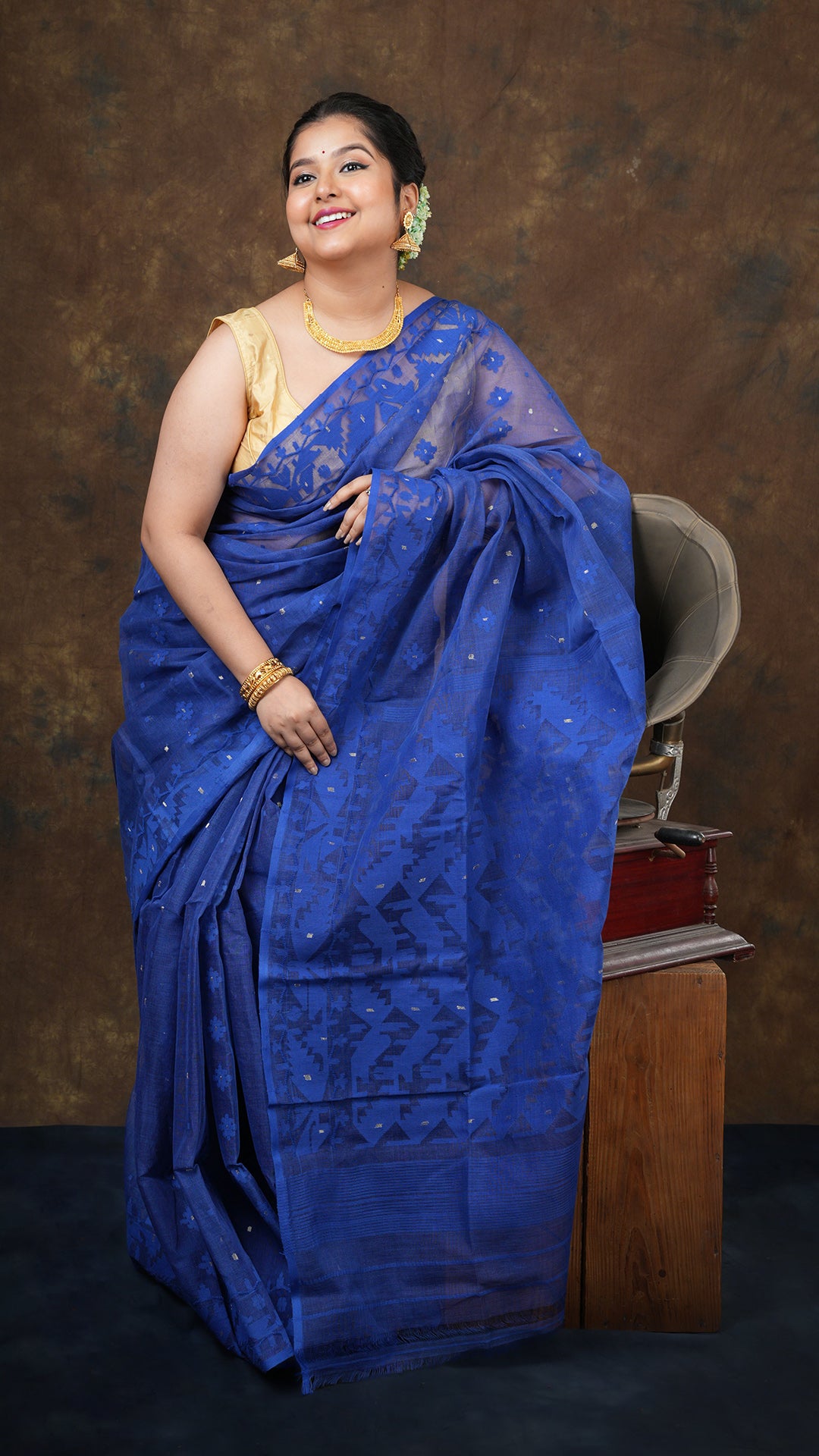 Dark blue cotton jamdani saree with self-colored and golden zari border, butis, and pallu. Includes 0.8m separate blouse piece. 5.5 meters.