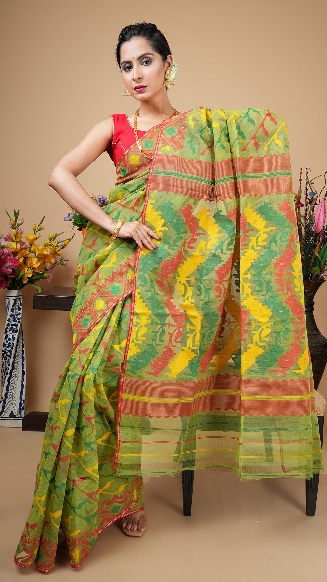 Green cotton Jamdani saree with red border accents, leheriya body design in red, yellow, and green, and traditional woven pallu. Statement wear for weddings or festive occasions.
