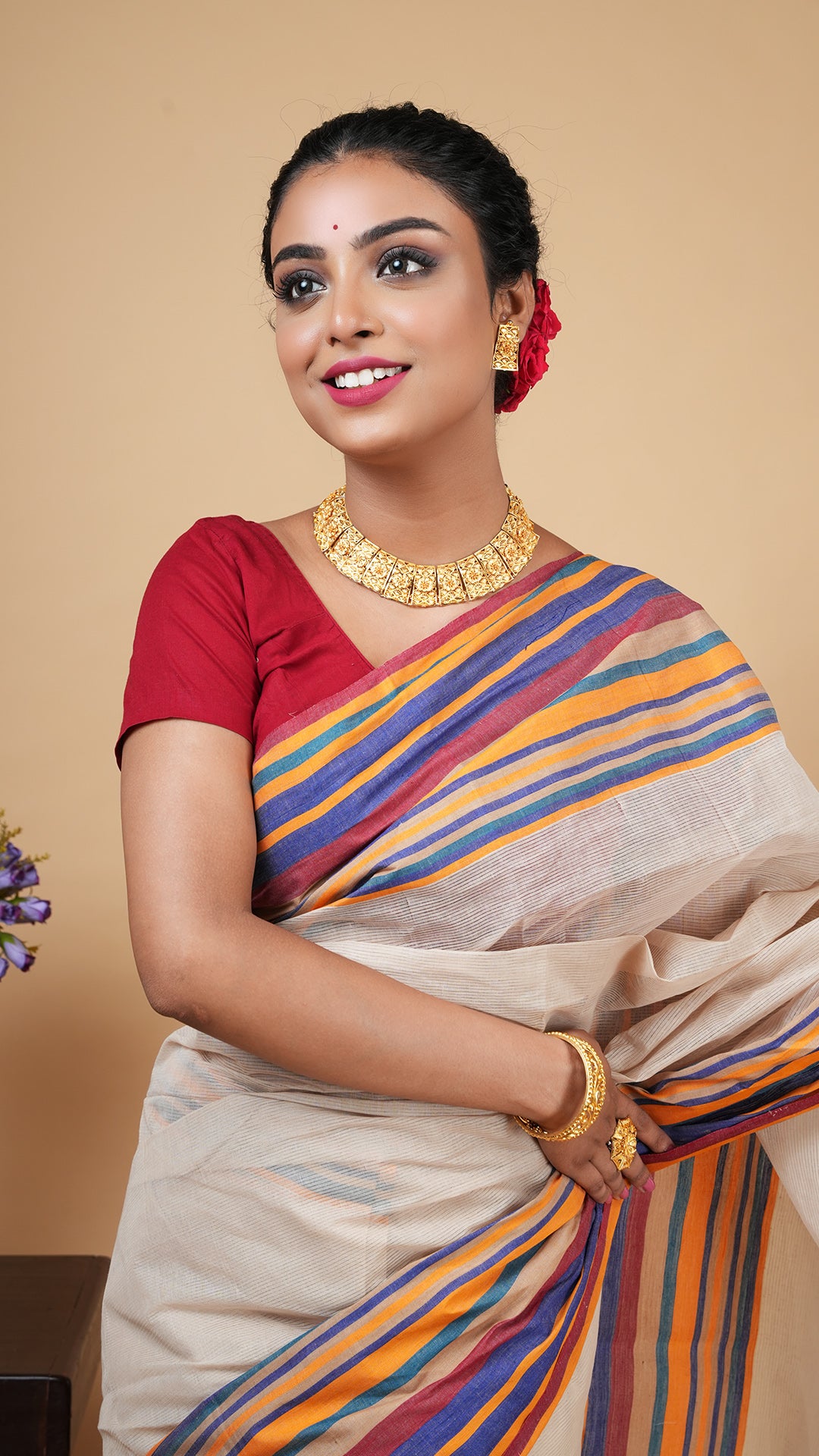 A close-up shot of a model wearing a light beige cotton saree, emphasizing the colorful striped border and the delicate self-stripe pattern.