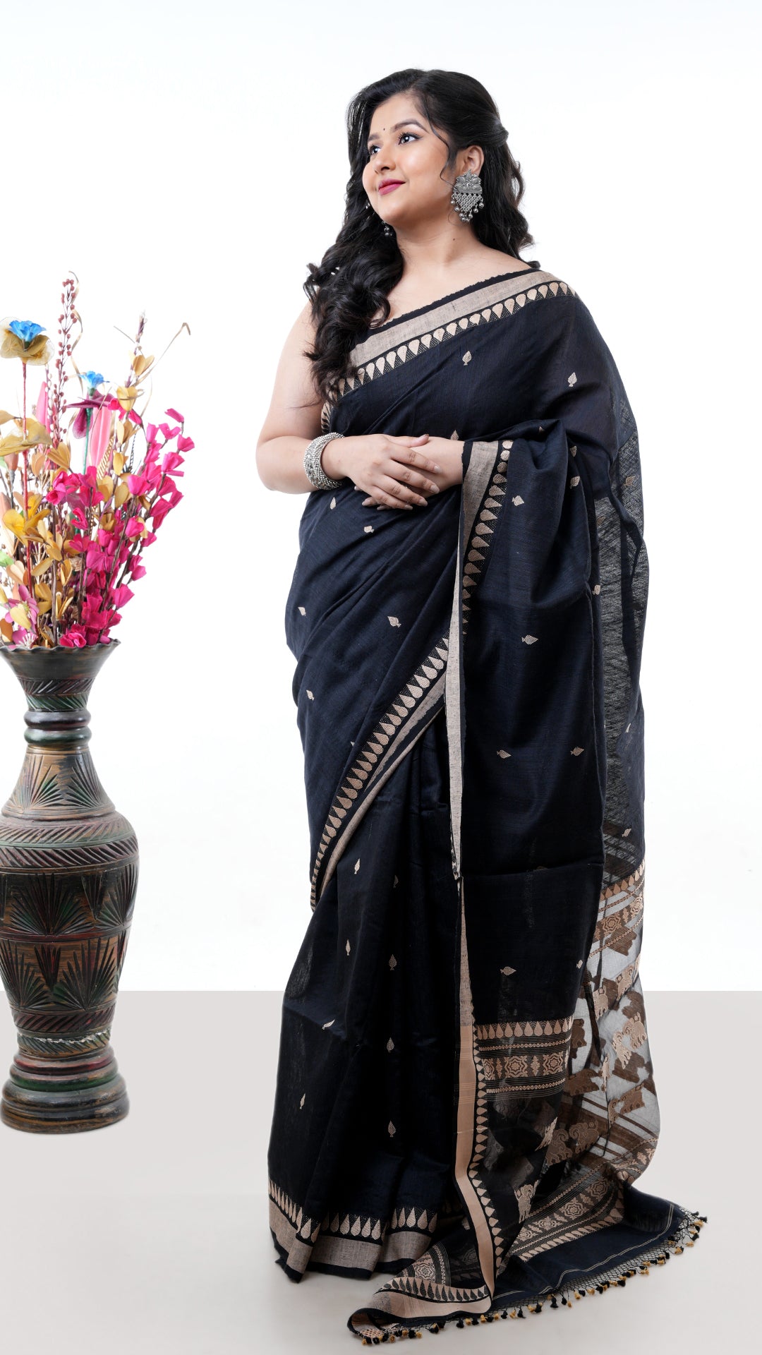 A black raw silk silk saree with beize weave. The pallu has textured black-beige weave. Crafted with muslin silk Warp and raw silk weft. Standard 5.5-meter length. Includes matching blouse piece. Tangail saree, handloom silk sari.