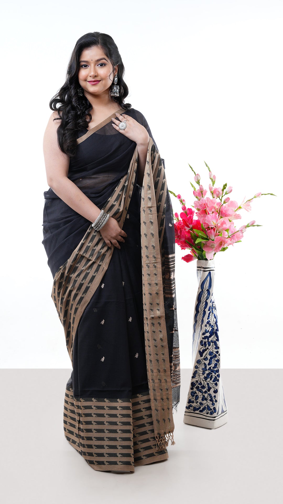 A black cotton saree. A soft cotton cotton saree in black colour. The border has temple-style detailing. Crafted with soft cotton Warp and weft. Standard 5.5-meter length. Includes matching blouse piece. Tangail saree, cotton saree.