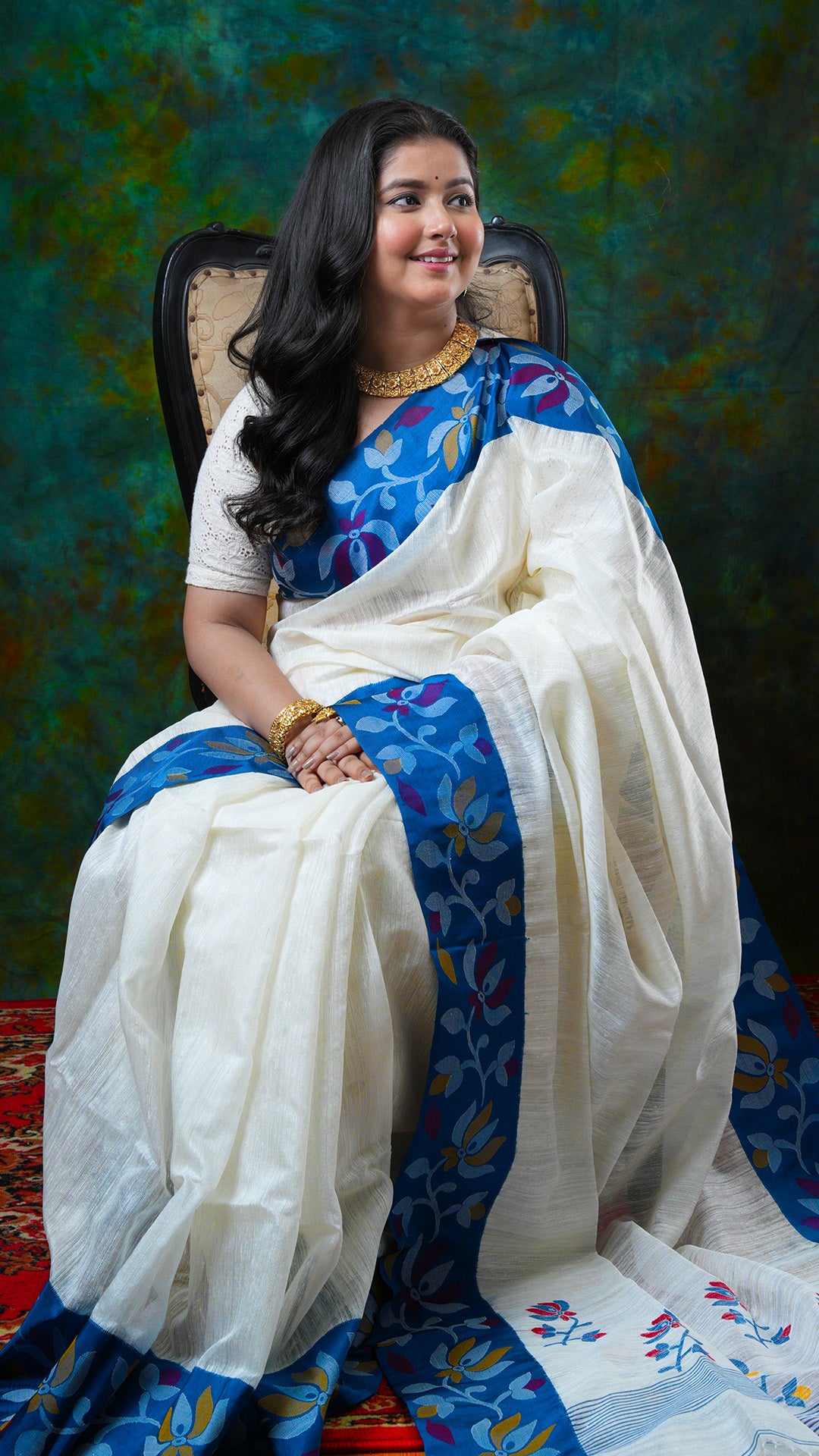Off-white raw silk saree with blue silk border, multicolored dhakai weave in red, yellow, and blue. Price: Rs. 16500/-