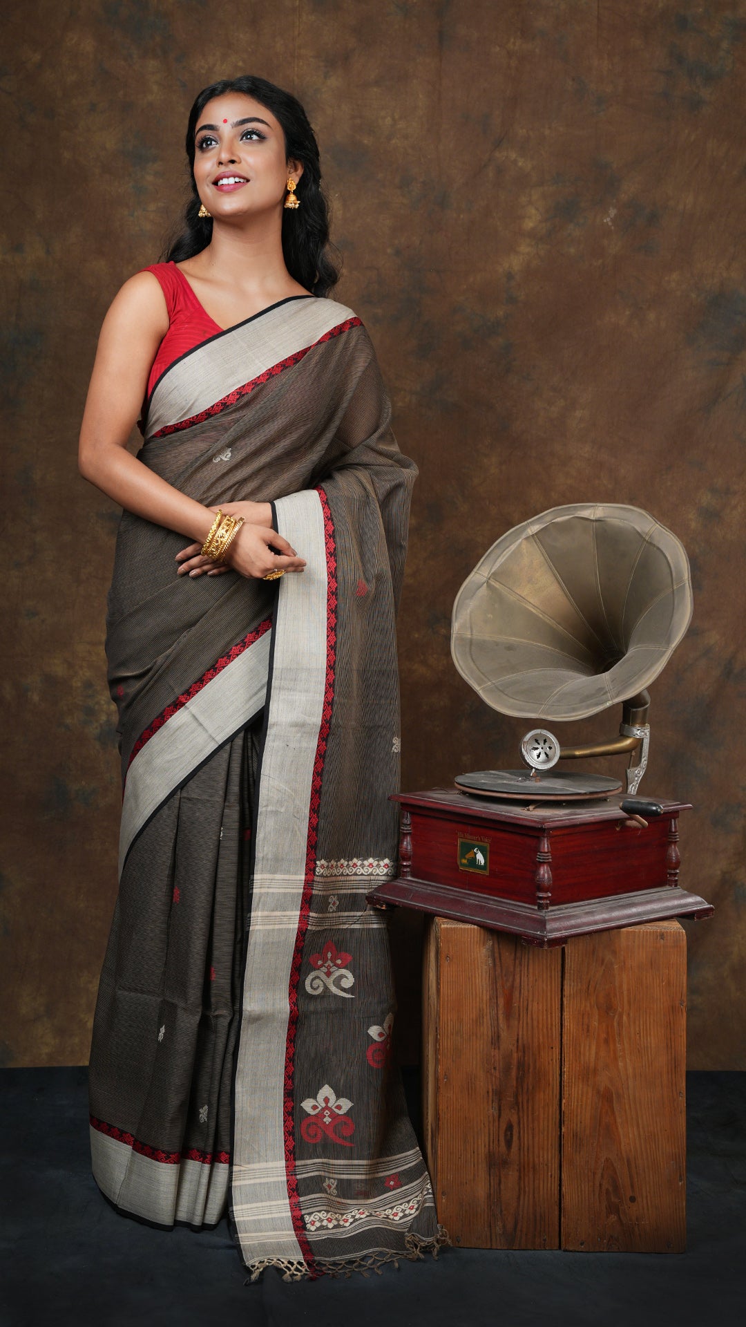 Black soft cotton tangail saree with beige stripes and butis throughout. Features beige and red woven border and pallu. Includes 0.8m running blouse. 5.5 meters
