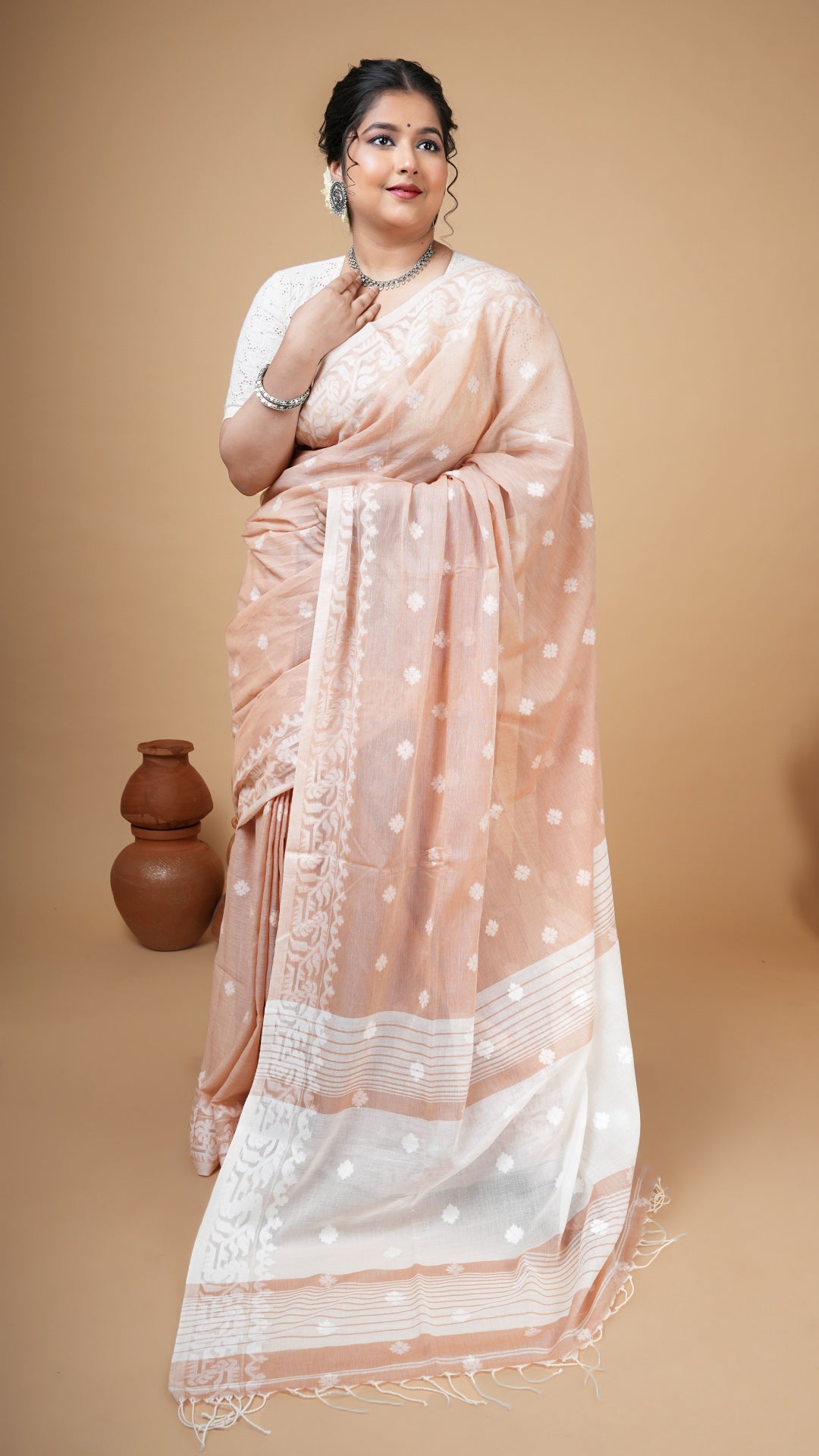 Beige machine-made dhakai saree with white woven butis and pallu. Soft cotton saree perfect for office and regular traditional wear.