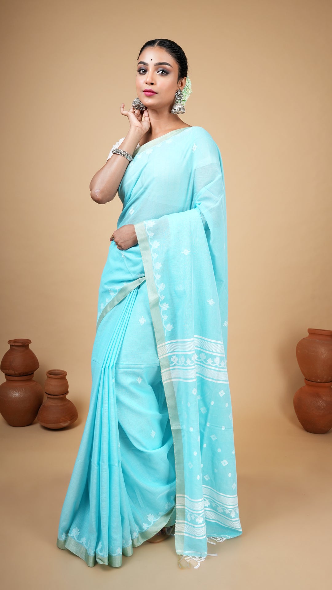 Firozi blue soft cotton tangail saree with white woven butis, pallu, and flat tassar border. Traditional saree for puja and gifting.